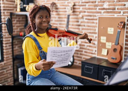 Femme africaine américaine musicienne jouant du violon regardant une feuille de musique dans un studio de musique Banque D'Images