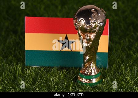 13 novembre 2022, Doha, Qatar. Trophée de la coupe du monde de la FIFA sur fond du drapeau du Ghana sur la pelouse verte du stade. Banque D'Images