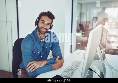 Faites-moi savoir ce que je peux faire pour vous. Portrait en grand angle d'un jeune homme d'affaires charmant portant un casque tout en étant assis à son bureau. Banque D'Images