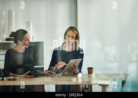 Et voici votre dernier jour. Une femme d'affaires enceinte et un collègue utilisant une tablette numérique ensemble dans un bureau. Banque D'Images