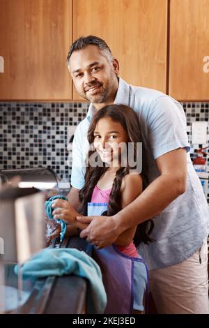 Papa et sis travaillent en équipe. Portrait d'un père et d'une fille joyeux laver les plats ensemble tout en regardant dans l'appareil photo dans la cuisine à Banque D'Images