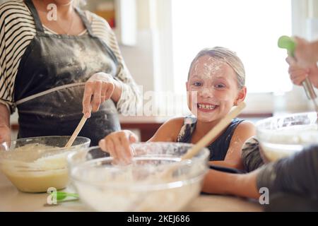 Le désordre est à moitié le plaisir. Deux petites filles qui cuisent avec leur mère dans la cuisine. Banque D'Images