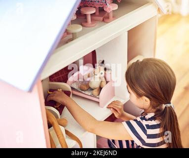 Jouer avec ses poupées. Photo en grand angle d'une petite fille jouant avec sa maison de poupée tout en étant assise sur le plancher de sa chambre. Banque D'Images