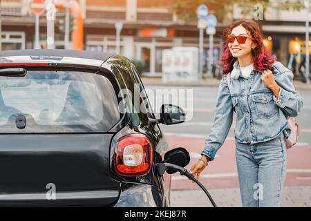 Une jeune fille heureuse charge son véhicule dans un parking gratuit pour les voitures éco-électriques dans la ville Banque D'Images