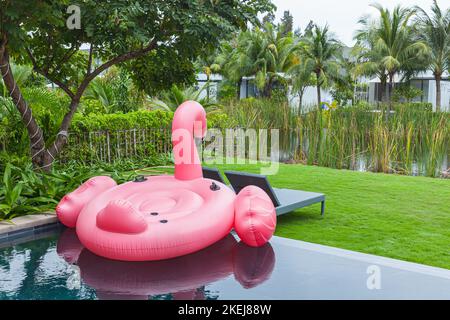 Flamant rose gonflable en plastique flottant sur la piscine avec jardin tropical Banque D'Images