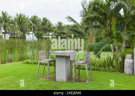 Béton, table de ciment et chaise en bois dans les tons gris neutres sur le terrain vert avec beaucoup d'arbres dans la journée ensoleillée Banque D'Images