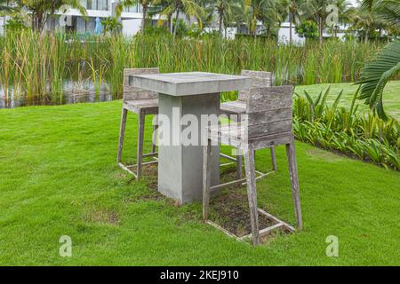 Béton, table de ciment et chaise en bois dans les tons gris neutres sur l'arrière-cour avec beaucoup d'arbres dans la journée ensoleillée Banque D'Images