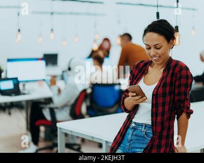 Une femme assise au bureau tient le smartphone sous le regard d'un ordinateur portable, synchronise les données entre l'ordinateur et le gadget au bureau, à l'aide des appareils de l'entreprise Banque D'Images