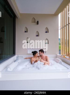 Couple buvant du champagne dans un jacuzzi pendant les vacances de lune de miel, femmes thaïes asiatiques et hommes caucasiens dans un jacuzzi de baignoire Banque D'Images