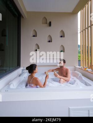 Couple buvant du champagne dans un jacuzzi pendant les vacances de lune de miel, femmes thaïes asiatiques et hommes caucasiens dans une baignoire jacuzzi sur le balcon Banque D'Images