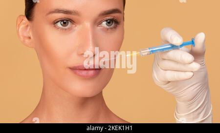 Concept d'injection de beauté. Gros plan des mains du médecin avec la seringue près du visage de la femme, panorama, fond beige Banque D'Images