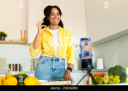 Blogging de nourriture. Excitée femme noire de tir sur le téléphone portable dans la cuisine, la cuisine et l'enregistrement vidéo, gestante ok Banque D'Images