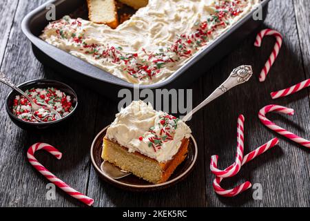 gâteau de noël en feuille de vanille avec glaçage à la crème fouettée garni de saupoudrés dans un plat de cuisson avec tranche sur une pelle à gâteau sur une table en bois sombre, Banque D'Images