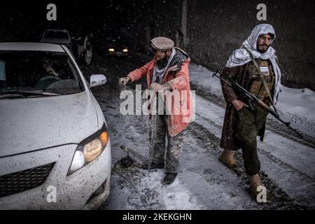 Col de Salang, Afghanistan. 13th novembre 2022. Un membre des talibans armé d'un fusil d'assaut AK-47 passe devant un ouvrier qui monte des chaînes de pneus sur un véhicule dans le tunnel de Salang tout en traversant l'Hindu Kush sur le col de Salang, le premier col de montagne reliant le nord de l'Afghanistan à la province de Parwan, avec des connexions vers la province de Kaboul. Credit: Oliver Weiken/dpa/Alay Live News Banque D'Images