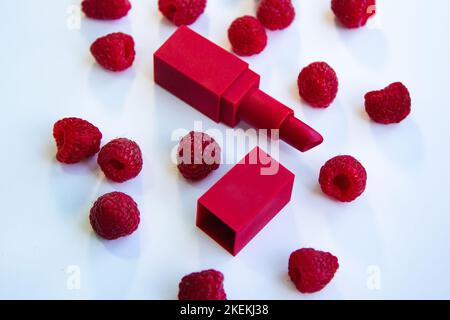 Rouge à lèvres brillant et framboises mûres juteuses sur fond blanc. Banque D'Images