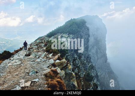 Randonnée pédestre solitaire sentier de montagne rocheux avec falaises rocheuses abruptes à proximité couvert de brouillard épais et de la Pologne, ville de Zakopane à distance dans les montagnes Tatra Banque D'Images