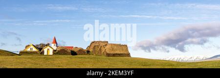 Panorama du village de Glaumbaer, Islande, avec des maisons traditionnelles recouvertes de gazon et une petite église en bois rouge et blanc et des montagnes enneigées i Banque D'Images