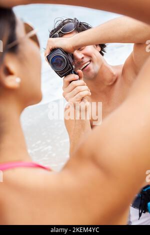 Homme et femme couple, petit ami de prendre des vidéos ou de filmer sa petite amie dans un bikini à la plage à l'aide d'un rétro appareil photo de film ciné vintage Banque D'Images