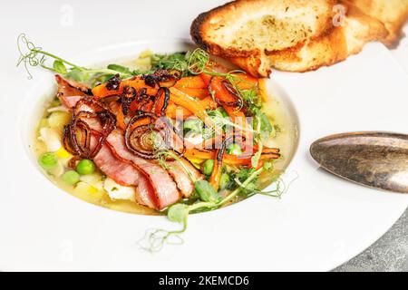 Fermez la soupe aux pois dans un bol blanc. Délicieuse soupe de légumes aux pois verts, aux carottes, au bacon frit et aux croûtons à l'ail. Banque D'Images