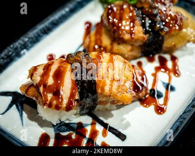 Deux sushis au foie gras avec sauce servis sur une assiette blanche sur une table sombre, de style japonais. Foie gras brûlé sur du riz à la prune aigre japonais. Banque D'Images