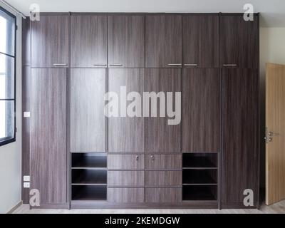 Grande armoire moderne en bois brun dans la chambre blanche, fermée, vue sur l'avant. Mobilier de placard intégré sur le mur près de la fenêtre dans le nouveau hou Banque D'Images