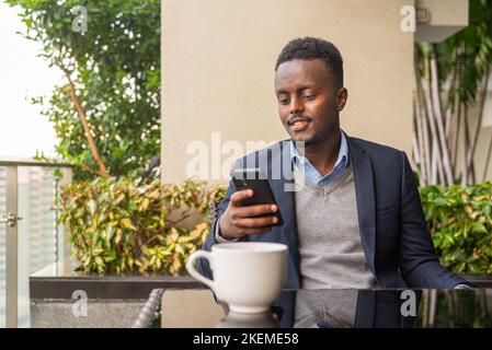 Portrait d'un beau homme d'affaires africain noir utilisant le téléphone et ayant une pause café Banque D'Images