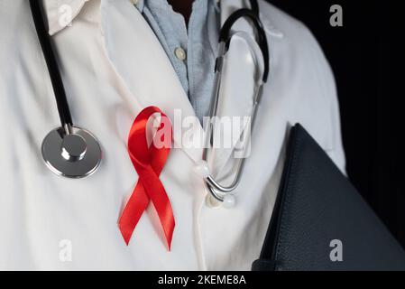 Gros plan d'un médecin portant un ruban rouge sur sa poitrine, symbole de la Journée mondiale du sida. Soutien du personnel de santé aux personnes vivant avec le vih. Prévention et fig. Banque D'Images