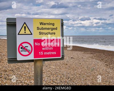 Un panneau d'avertissement rouge et jaune sur une plage de galets à la Sluice sur la côte du Suffolk avertit d'une structure submergée et que la baignade n'est pas autorisée. Banque D'Images