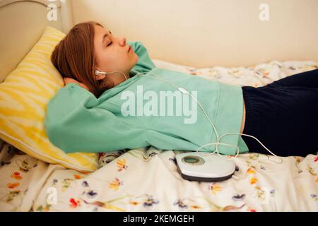 Une adolescente présente un CD et écoute de la musique dans sa chambre. Fille avec joueur rétro Banque D'Images