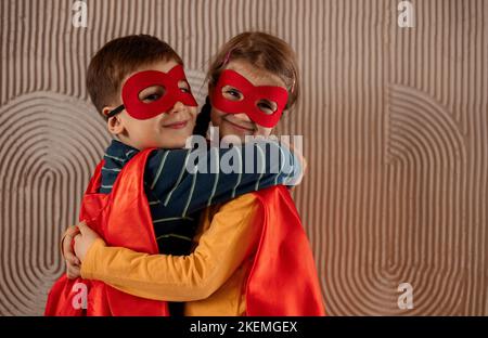 Portrait d'une équipe de deux jeunes super-héros, frère et sœur, sur fond beige. Enfant super-héros. Super héros gamin jouant à la maison. Idée, liberté Banque D'Images