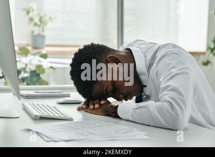 Homme d'affaires afro-américain fatigué dormant sur le lieu de travail devant un ordinateur au bureau Banque D'Images