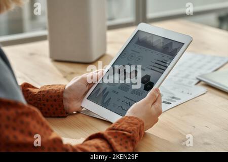 Gros plan d'une femme d'affaires examinant des graphiques sur l'écran d'un Tablet pc tout en étant assise à table au bureau Banque D'Images