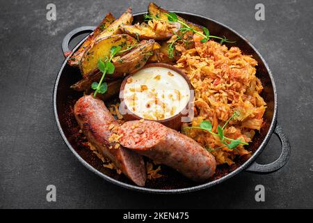 Saucisses frites avec pommes de terre et chou, sur une poêle, sur fond sombre Banque D'Images