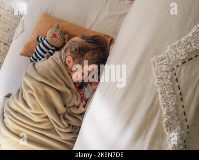 Adorable petite fille dort sur le canapé à côté de son animal en peluche préféré Banque D'Images