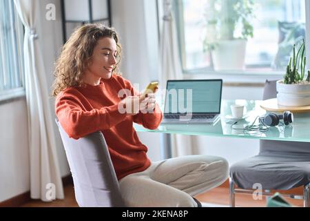 Jeune femme souriante utilisant un téléphone portable étudiant ou travaillant à la maison. Banque D'Images