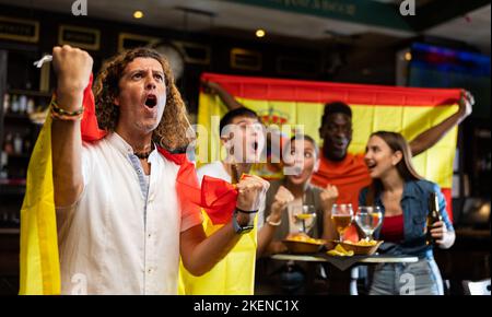 Des supporters sportifs internationaux heureux qui arborent le drapeau de l'Espagne et boivent de la bière au pub Banque D'Images