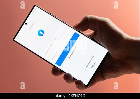 New york, Etats-Unis - 10 novembre 2022 : inscrivez-vous sur Facebook sur votre smartphone en gardant à la main un gros plan sur fond rose Banque D'Images