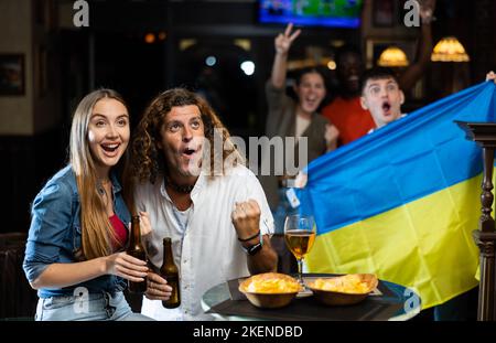 Couple expressif qui s'adresse à l'équipe ukrainienne favorite dans le bar sportif Banque D'Images