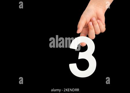 numéro trois à la main, isolé sur fond noir. Numéro trois dans la main d'un enfant sur fond noir. À insérer dans un projet ou une conception. Banque D'Images