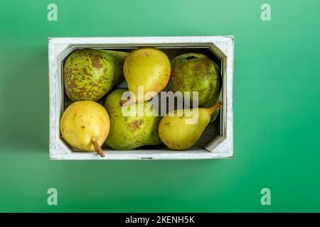 Vue de dessus image d'une caisse en bois peinte en blanc pleine de poires mûres de différentes variétés sur fond vert Uni Banque D'Images