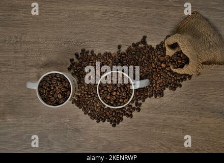 Vue de dessus des grains de café torréfiés bruns déversés sur une table avec une tasse de café pleine, image Banque D'Images