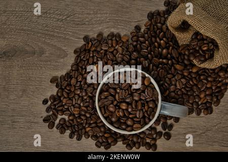 Vue de dessus des grains de café torréfiés bruns déversés sur une table avec une tasse de café pleine, image Banque D'Images