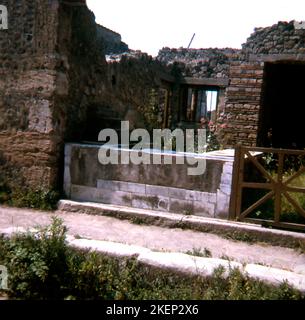 L'éruption du Mt. 79 de l'A.D. Vésuve enterra la ville romaine de Pompéi. Les fouilles se poursuivent maintenant sur le site. Parmi les zones découvertes se trouvent les maisons qui avaient des vitrines au rez-de-chaussée, comme celle qui avait des amphores dans les comptoirs. Les marchandises auraient été conservées dans les amphores. Cette pratique des magasins autour du périmètre extérieur d'une maison était commune. Souvent, le commerçant et sa famille vivaient à l'arrière du magasin. Certains avaient même des lofts pour la salle de séjour, notez les escaliers à gauche sur cette photo. Banque D'Images