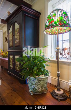 Plante verte en pot et lampe sur pied en verre teinté à côté d'une armoire en bois avec des scènes peintes sur les portes dans le coin du salon à l'intérieur de la vieille maison. Banque D'Images