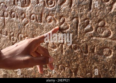 Index d'un homme montrant l'ancien script tamoul sculpté sur le mur du temple de Tanjore Brihadeeswarar. Banque D'Images