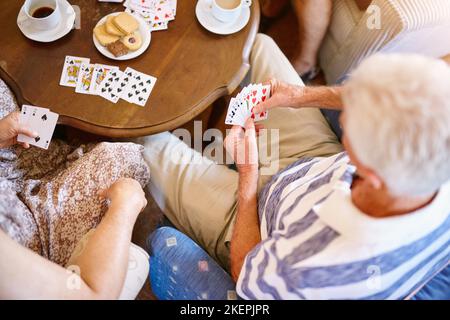 Jouer les cartes distribuées. Photo en grand angle d'un groupe d'aînés jouant des cartes autour d'une table dans leur maison de retraite. Banque D'Images