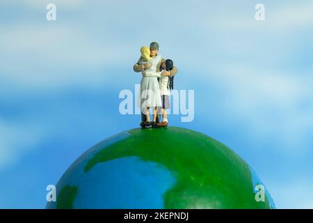 Photographie miniature de personnage de jouet de personnes. Concept de journée de réunion de famille. Père embrassant sa femme et sa fille au-dessus du globe terrestre. Photo d'image Banque D'Images