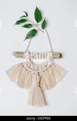 Magnifique macrame sur bâton suspendu sur un mur blanc, décoré de feuilles. Banque D'Images
