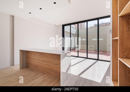 L'intérieur vide de l'appartement rénové avec la lumière naturelle qui brille à travers de grandes fenêtres. Cuisine moderne avec îlot et mobilier en bois. Banque D'Images