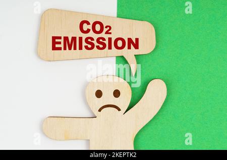 Concept environnemental. Sur fond vert et blanc, une triste figure en bois d'un homme et une plaque avec l'inscription - CO2 Emission Banque D'Images